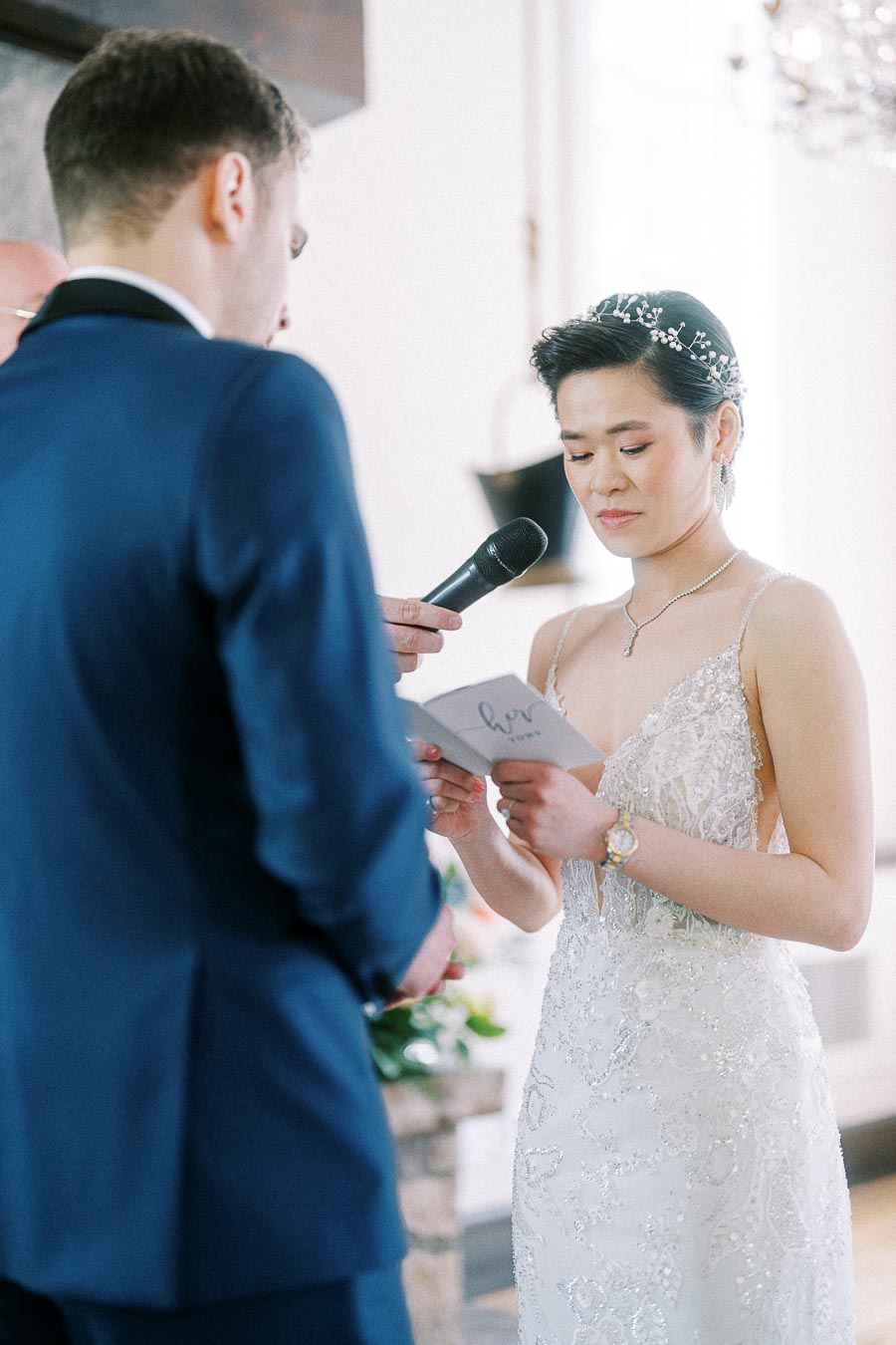 Bride reads wedding vows from a card while standing before the groom during an indoor ceremony.