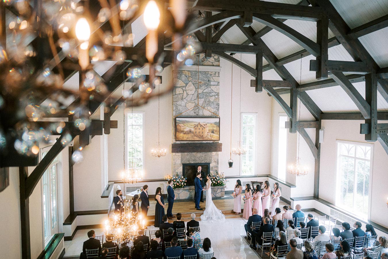 Wide view of Miffy and Rawle at the altar in Ancaster Mill’s timber-beamed chapel with wedding party and seated guests.