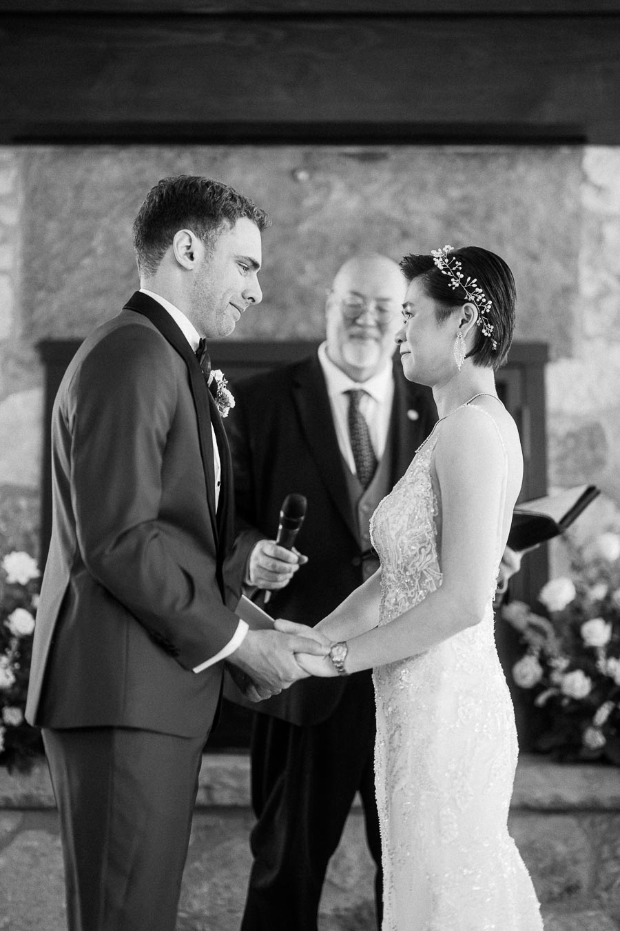Miffy and Rawle hold hands during their indoor wedding ceremony with an officiant standing behind them.