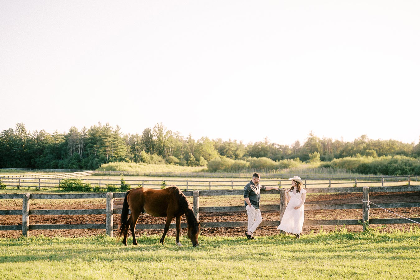 Expectant couple beside a grazing horse at The Green Acres in Flamborough, Ontario