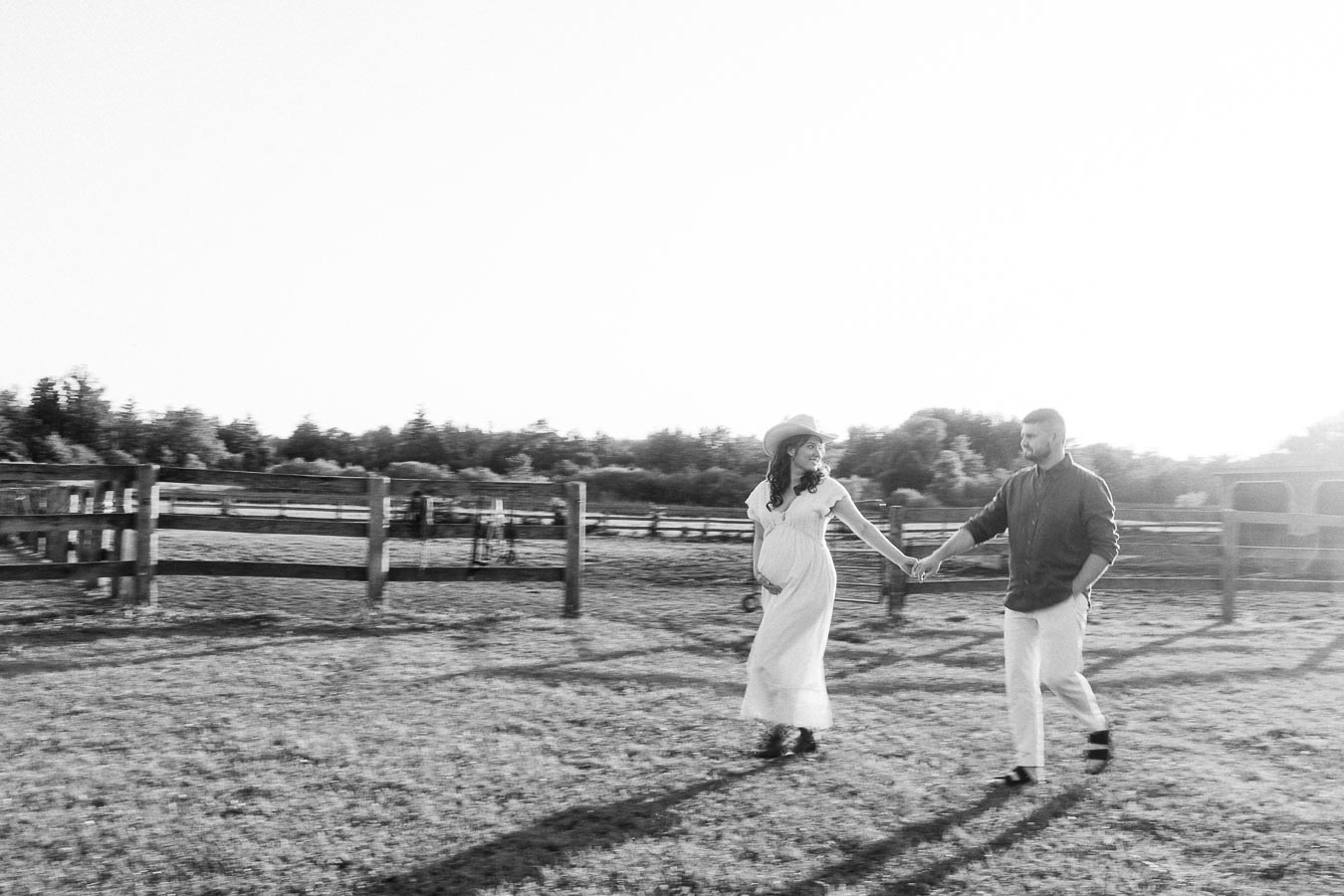 Expectant couple holding hands in a fenced farm paddock at The Green Acres