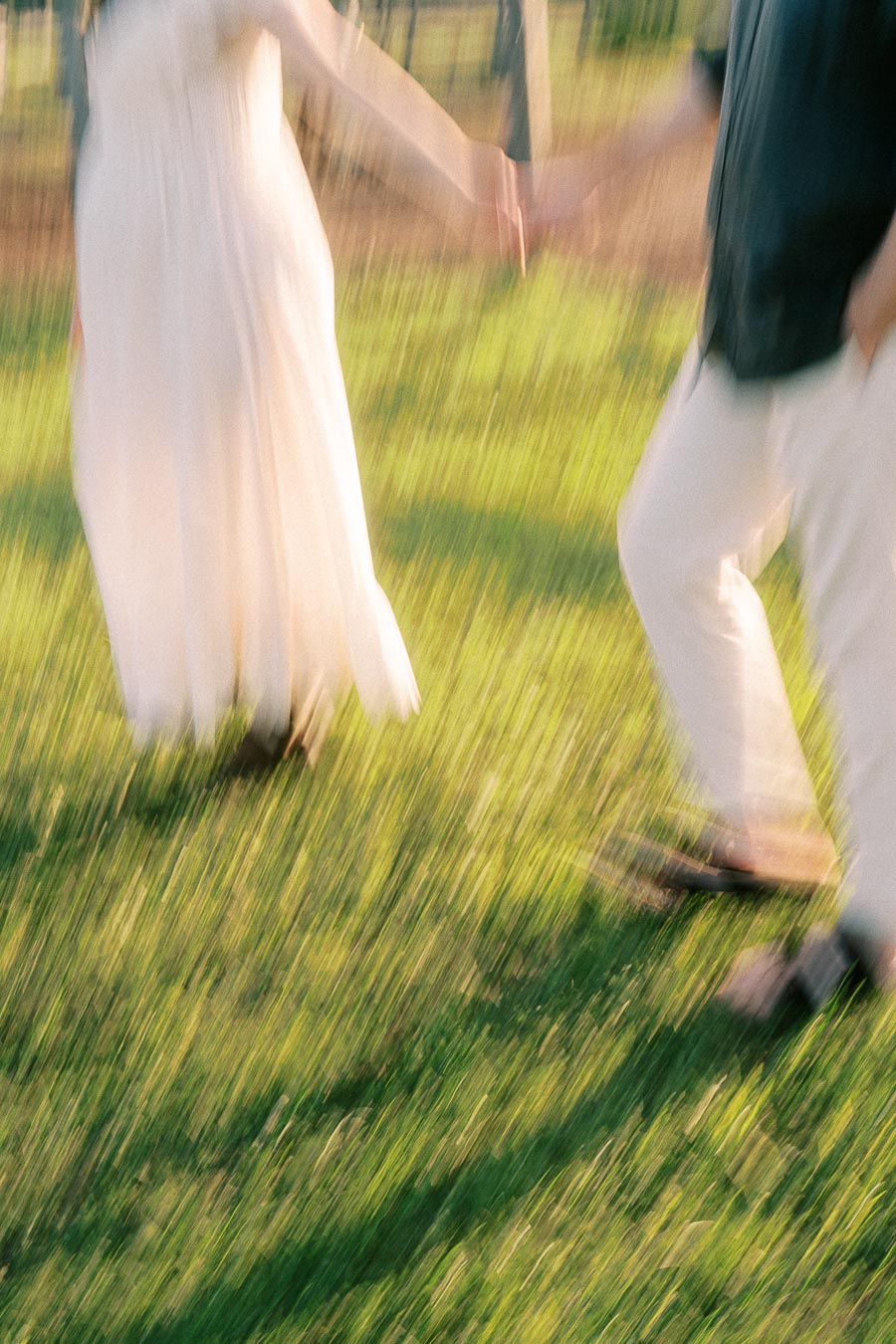 Expectant couple holding hands while walking through grass at The Green Acres