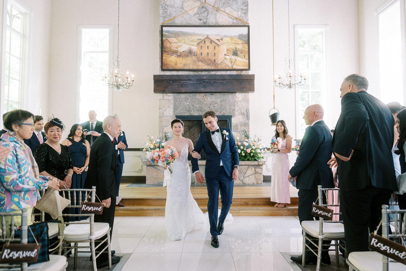 Bride and groom walk arm in arm down the aisle as guests stand inside the Ancaster Mill chapel.