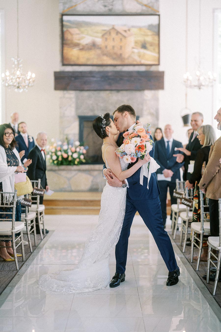 Bride and groom kiss in the ceremony aisle while guests watch and smile inside Ancaster Mill.