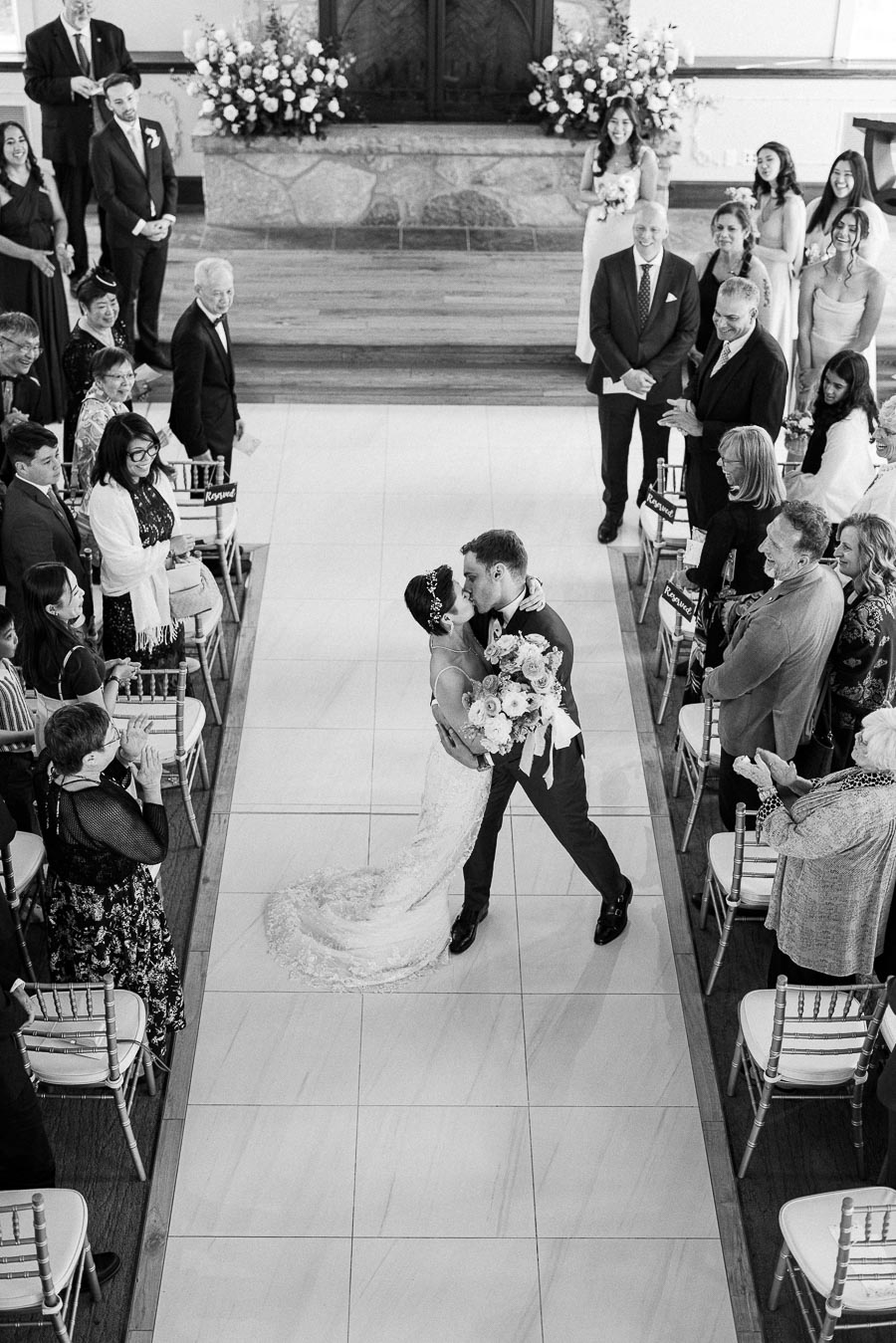 Miffy and Rawle kiss in the chapel aisle as guests applaud after their wedding ceremony.