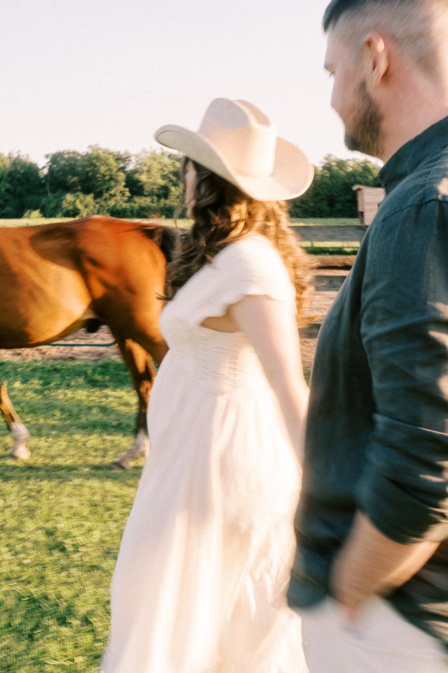 Pregnant woman in white dress and cowboy hat walking beside a horse