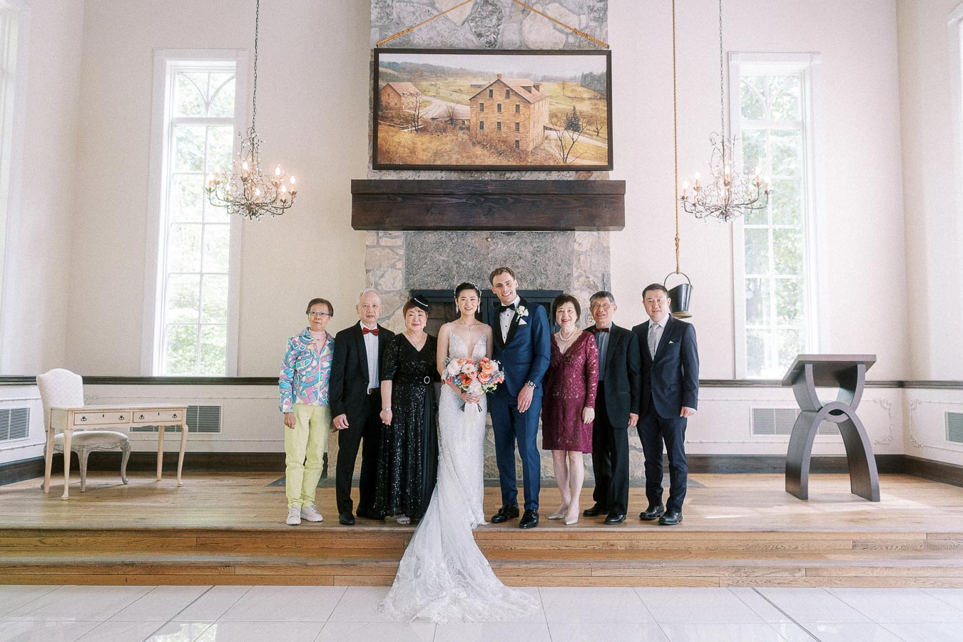 Miffy and Rawle stand with family on a chapel stage in front of a stone fireplace and chandeliers.