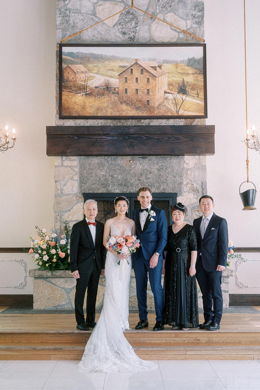 Miffy and Rawle pose with four family members in formal attire before a stone fireplace at Ancaster Mill.