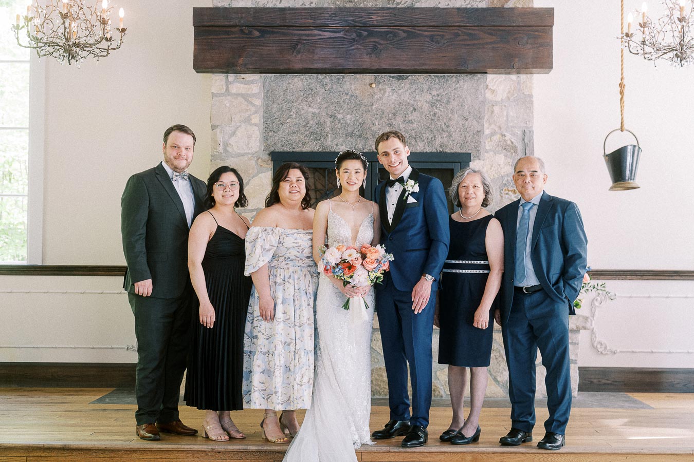 Bride and groom pose with family in front of a stone fireplace at Ancaster Mill.
