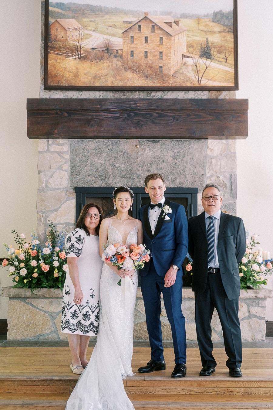 Miffy and Rawle pose with her parents beside a stone fireplace with flowers at Ancaster Mill.