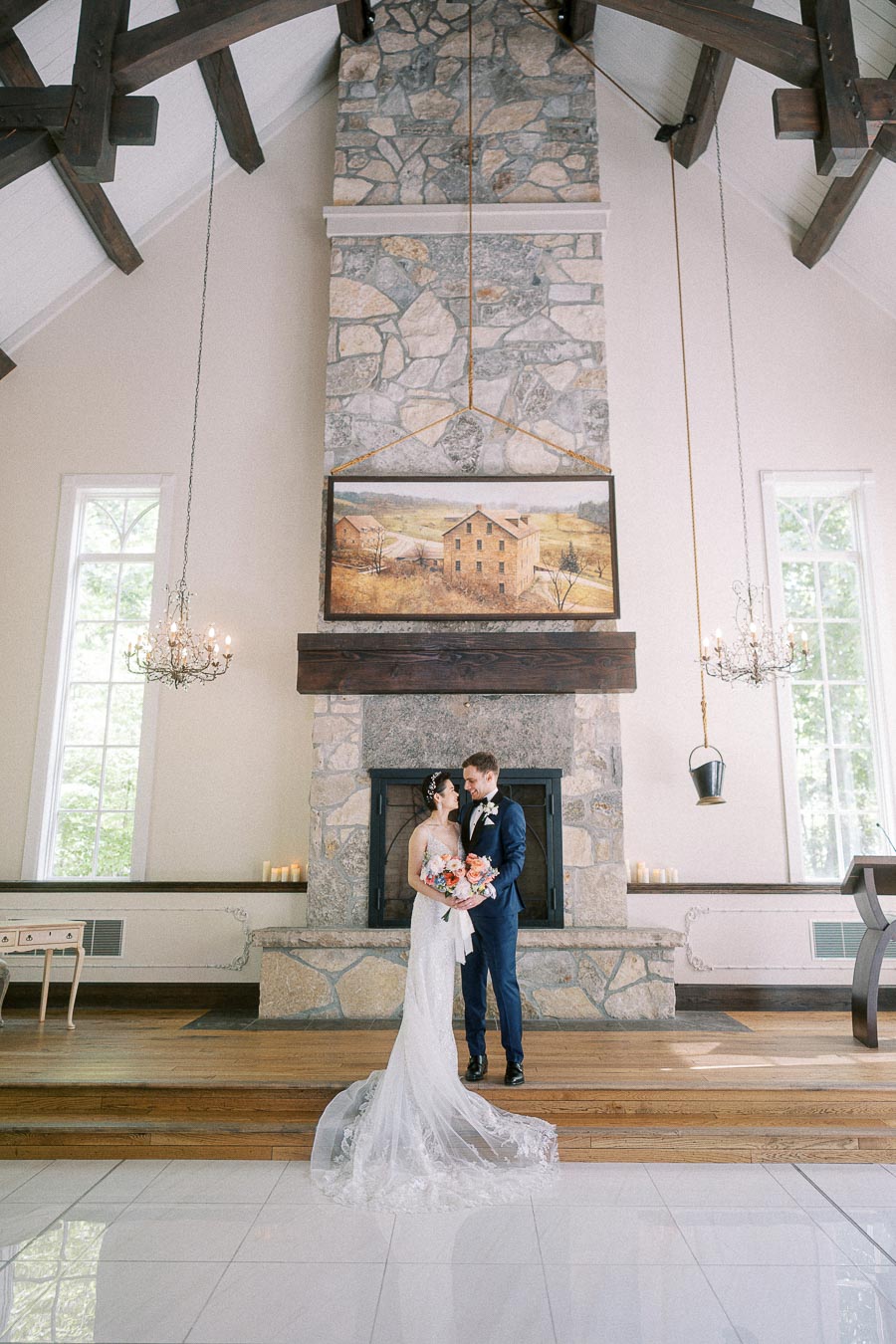 Bride and groom stand together before a tall stone fireplace inside Ancaster Mill chapel.
