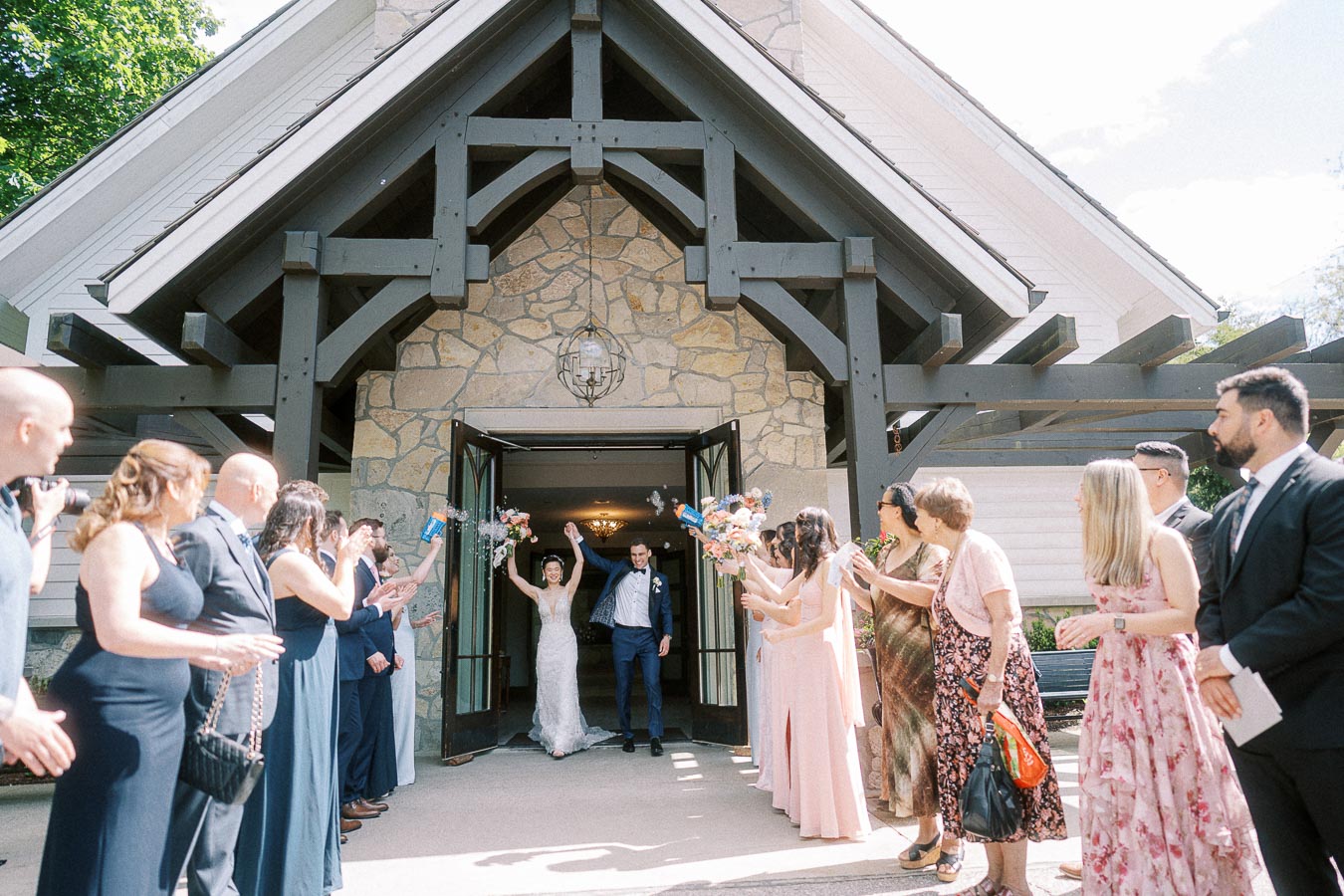 Miffy and Rawle exit the Ancaster Mill chapel as guests cheer and blow bubbles outside the stone entrance.
