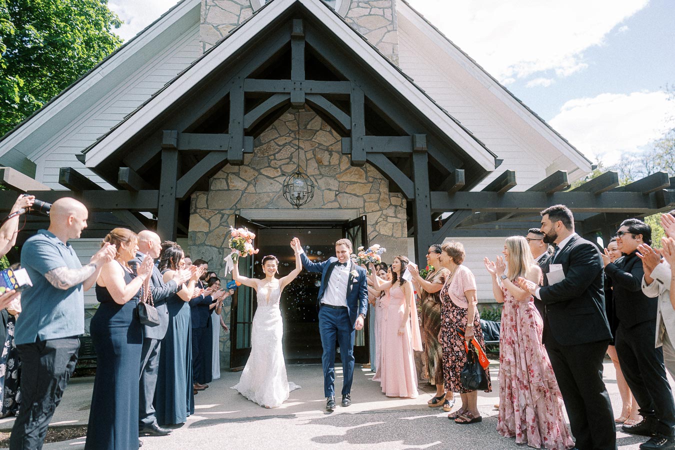 Miffy and Rawle exit the chapel hand in hand as guests clap and toss petals outside Ancaster Mill.