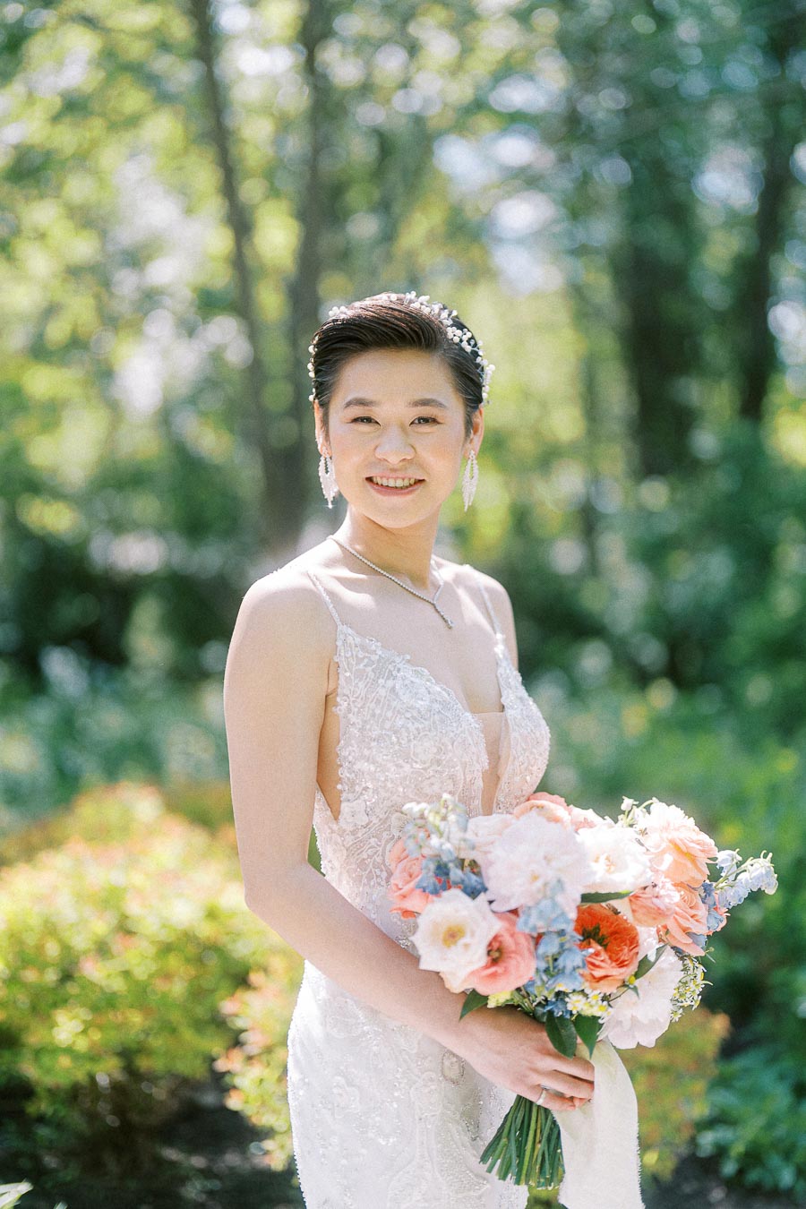 Miffy smiles outdoors in a lace wedding gown, holding a pastel bouquet in a sunlit garden.