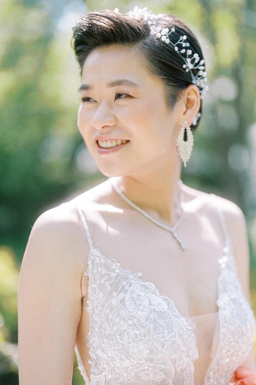 Bride Miffy smiling outdoors in a beaded wedding gown with pearl hairpiece, earrings, and necklace