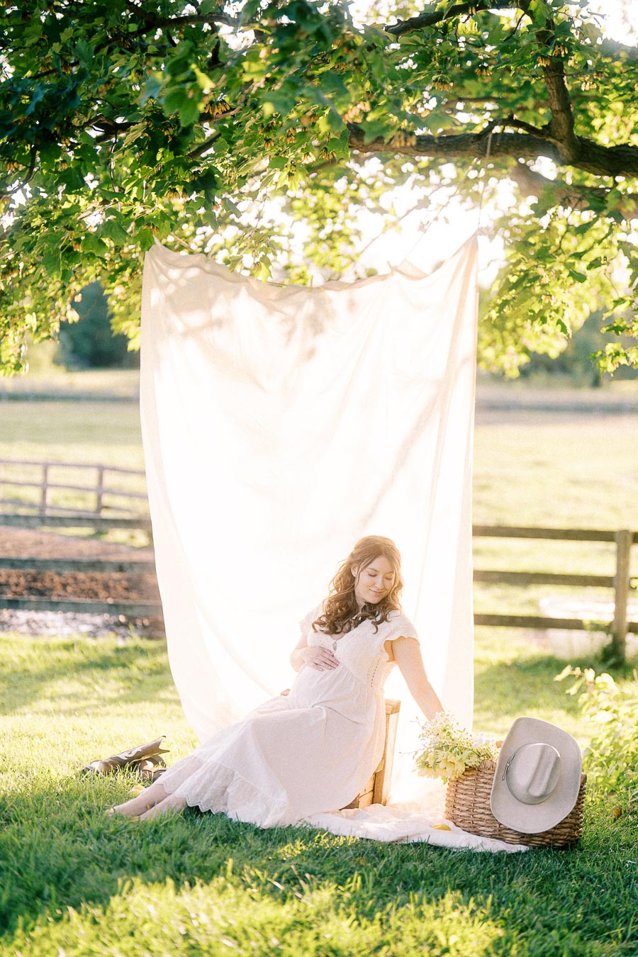 Pregnant woman in white dress seated under a tree at The Green Acres
