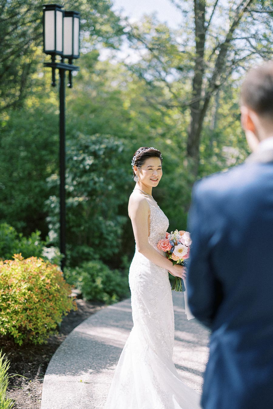 Bride Miffy smiles in a fitted white gown while holding a bouquet during an outdoor first look with Rawle.
