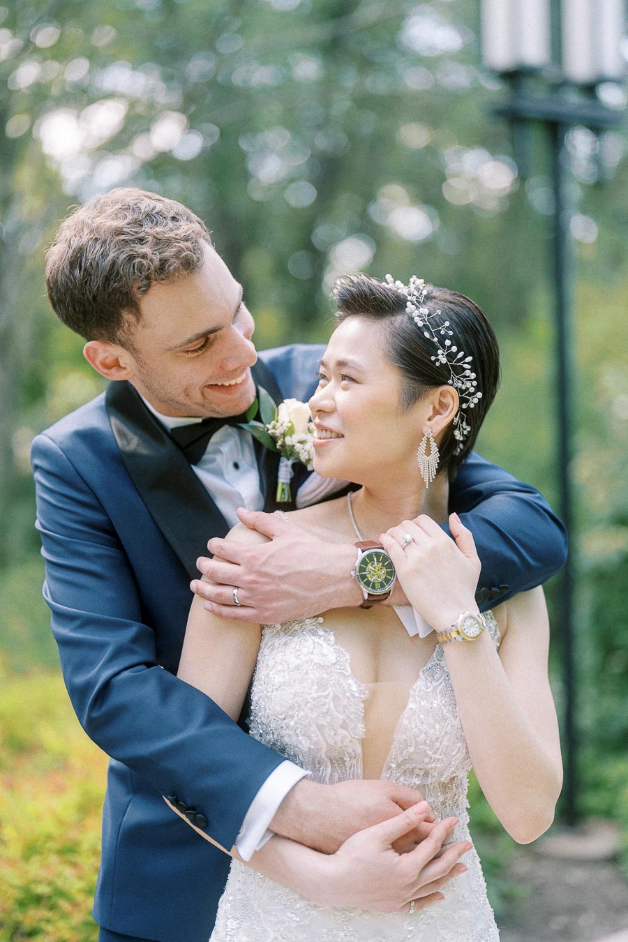 Miffy and Rawle smiling together in wedding attire outdoors, with Rawle embracing Miffy from behind.