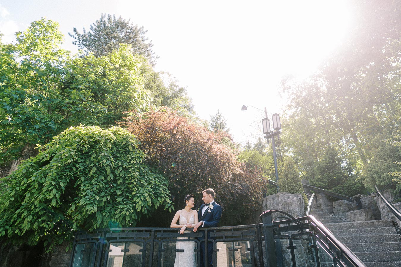 Miffy and Rawle stand on a terrace railing surrounded by trees and stone stairs in bright sun.