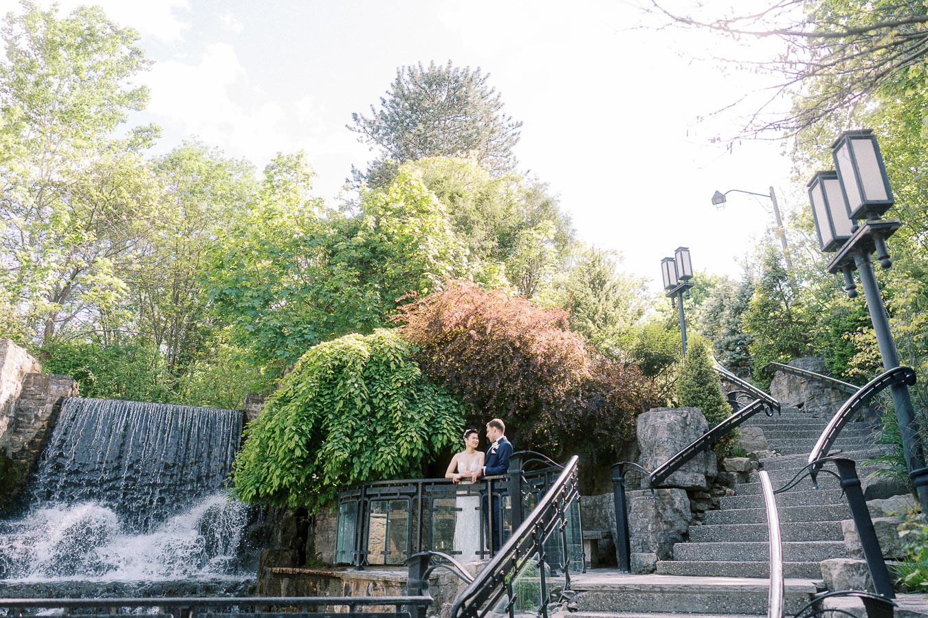 Miffy and Rawle stand together on a bridge beside a waterfall and stone steps at Ancaster Mill.