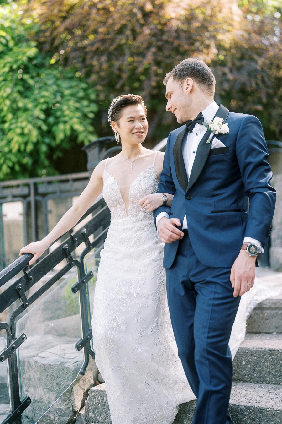 Bride in lace gown and groom in navy tuxedo walking arm in arm down outdoor stone steps