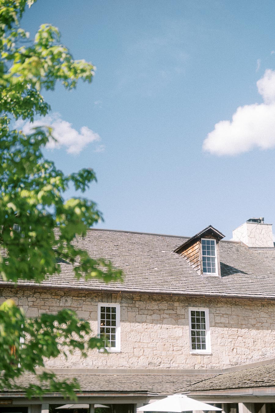 Stone building roof and white windows at Ancaster Mill framed by green leaves under a blue sky