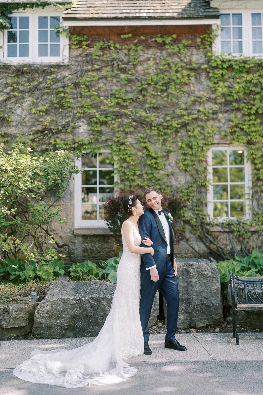Bride and groom stand arm in arm outside an ivy-covered stone building at Ancaster Mill.