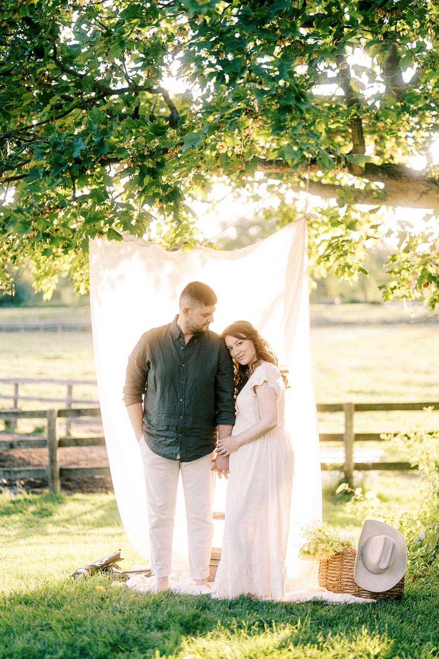Expectant couple posing under a leafy tree at The Green Acres