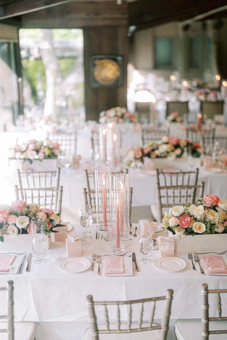Reception tables with pastel floral centerpieces, pink candles, white linens, place settings, and silver chairs