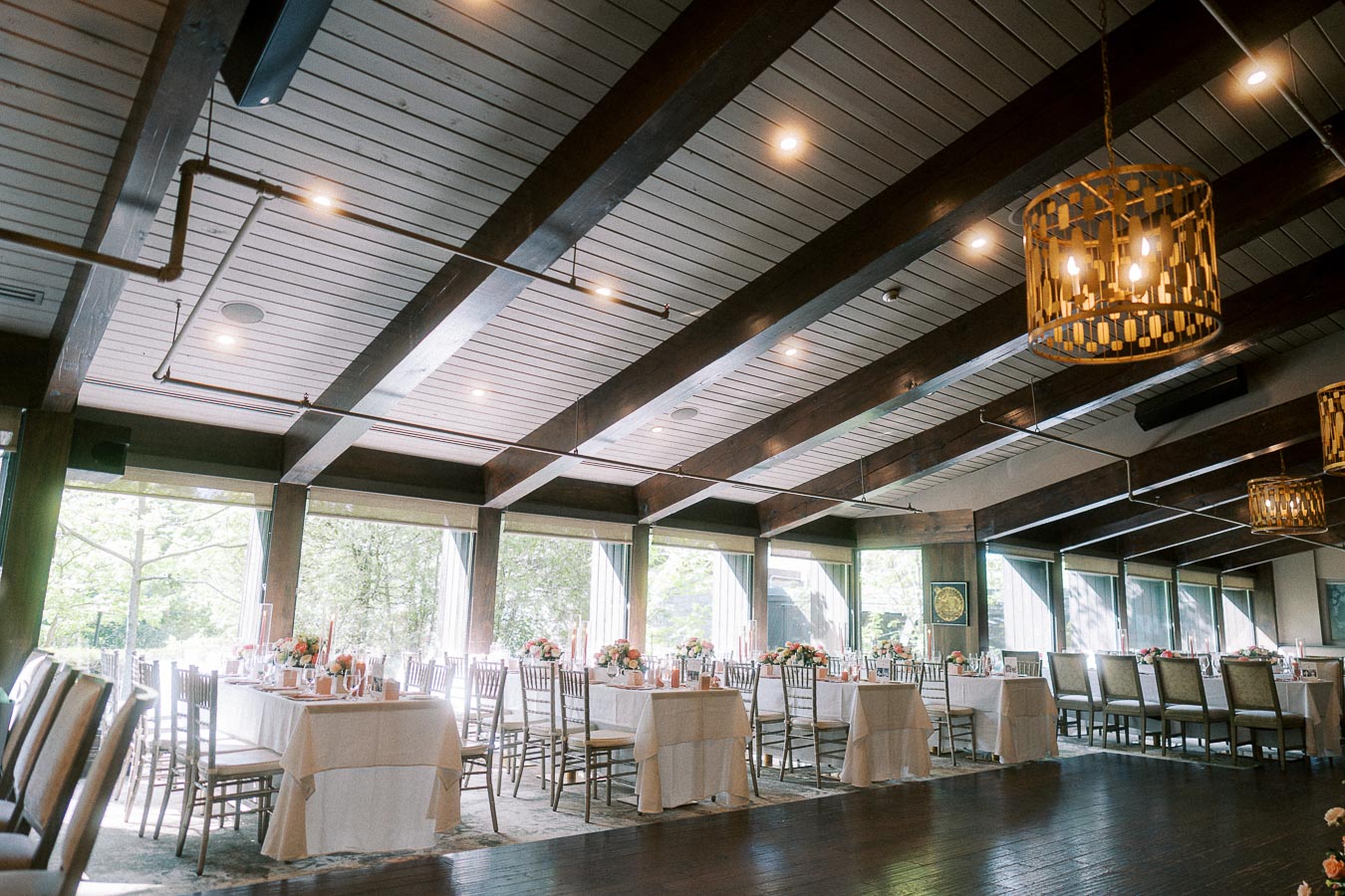 Elegant reception room with round tables, floral centerpieces, wood beams, and pendant lights at Ancaster Mill.