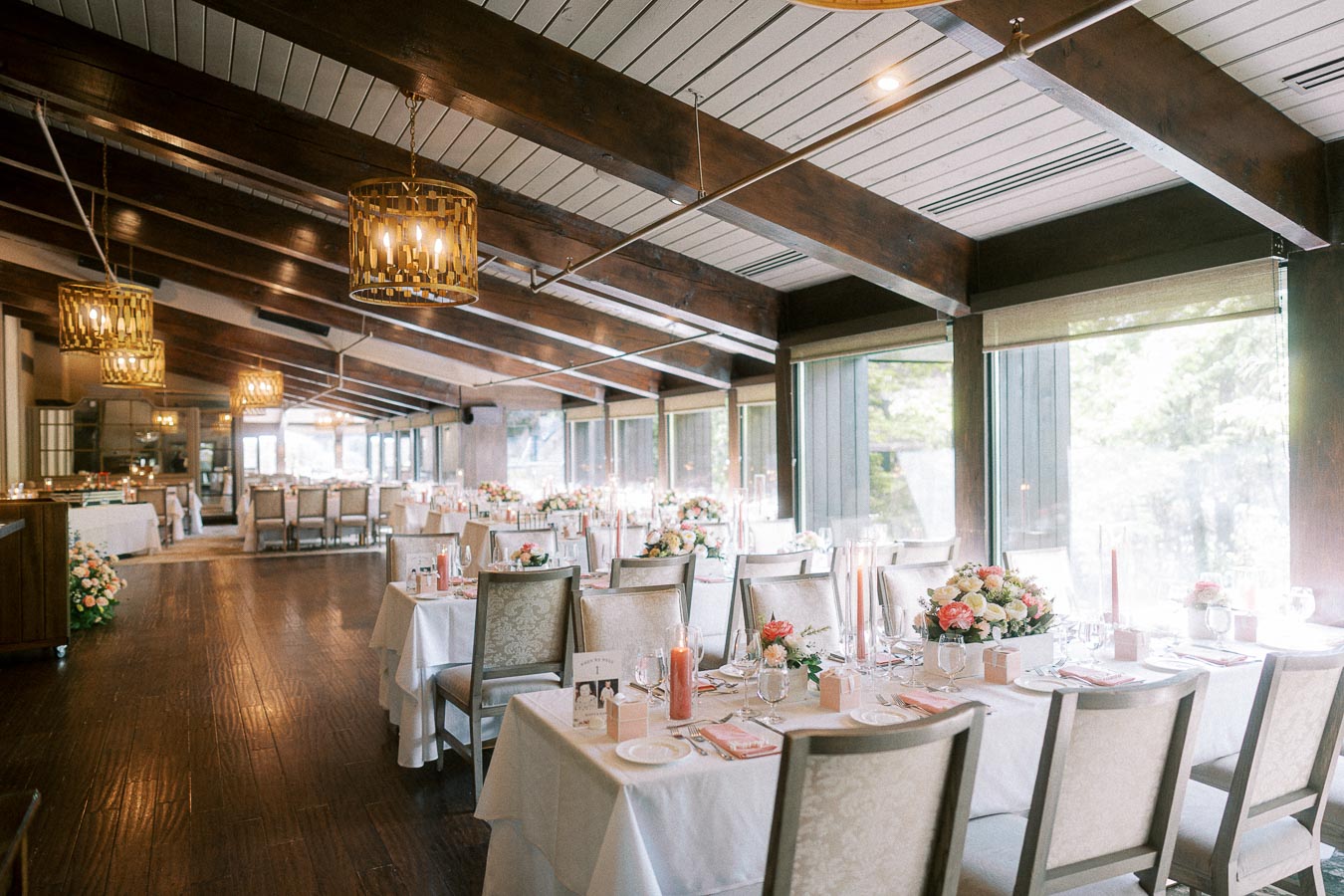 Elegant wedding reception room with long tables, floral centerpieces, candles, chandeliers, and large windows at Ancaster Mill.