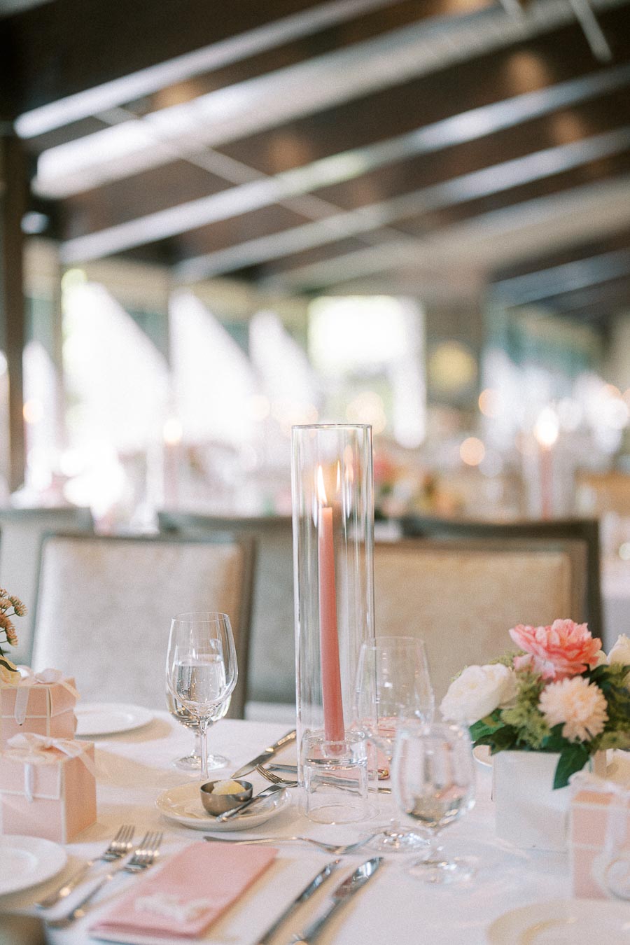 Reception table with pink taper candle, floral centerpieces, glassware, napkins, and favor boxes