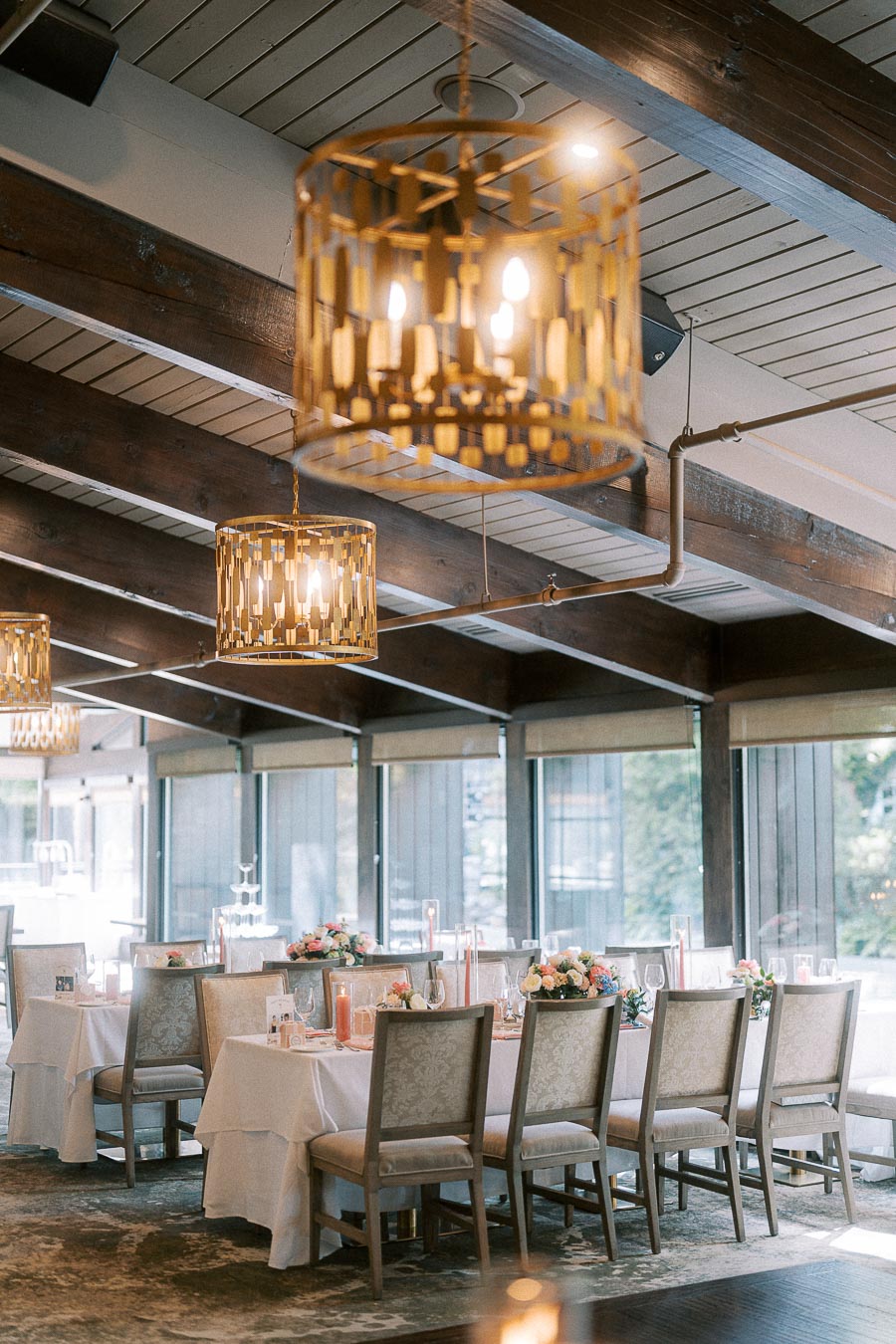 Reception tables with floral centerpieces beneath gold pendant lights and wood beams at Ancaster Mill.