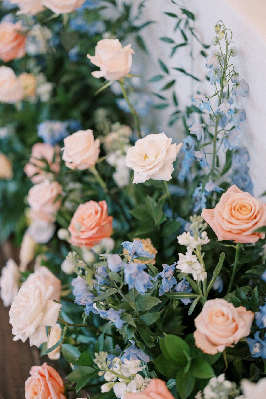 Peach and ivory roses with pale blue flowers and greenery in a soft wedding floral arrangement.