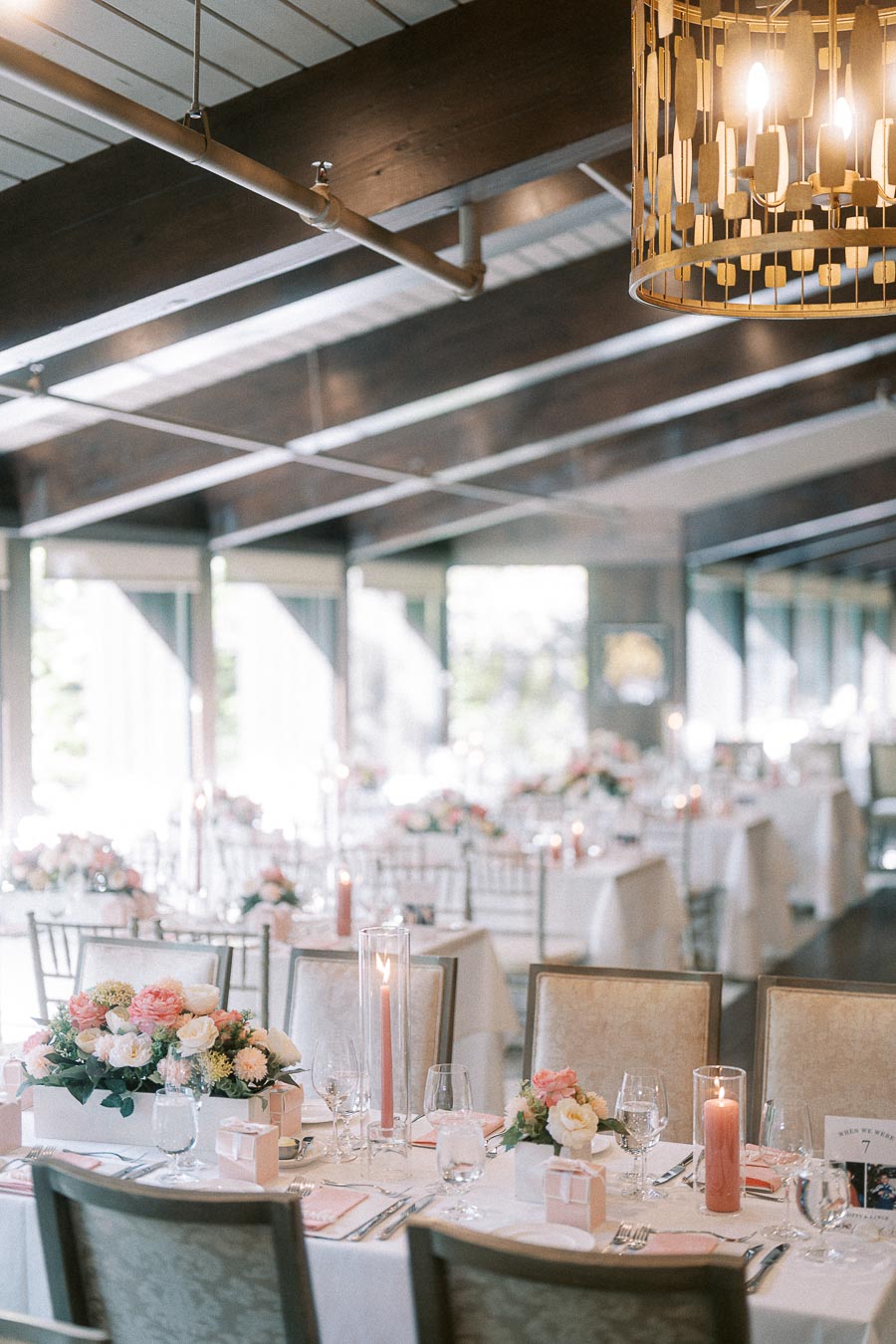 Reception tables with pastel flowers, pink candles, place settings, and chandeliers inside Ancaster Mill