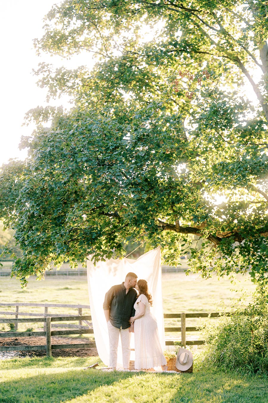Expectant couple kissing beneath a tree at The Green Acres in Flamborough, Ontario