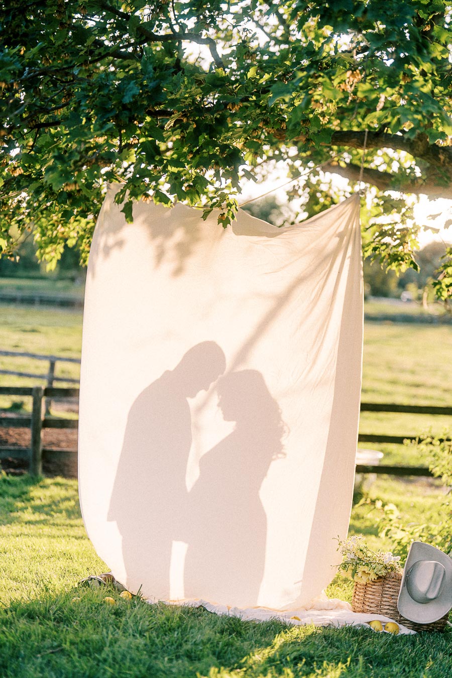 Expectant couple’s silhouettes behind fabric in a farm setting at The Green Acres