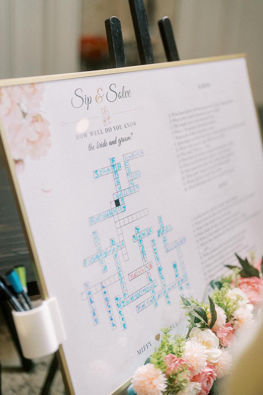 Framed Sip and Solve wedding crossword with markers and pastel flowers at the reception