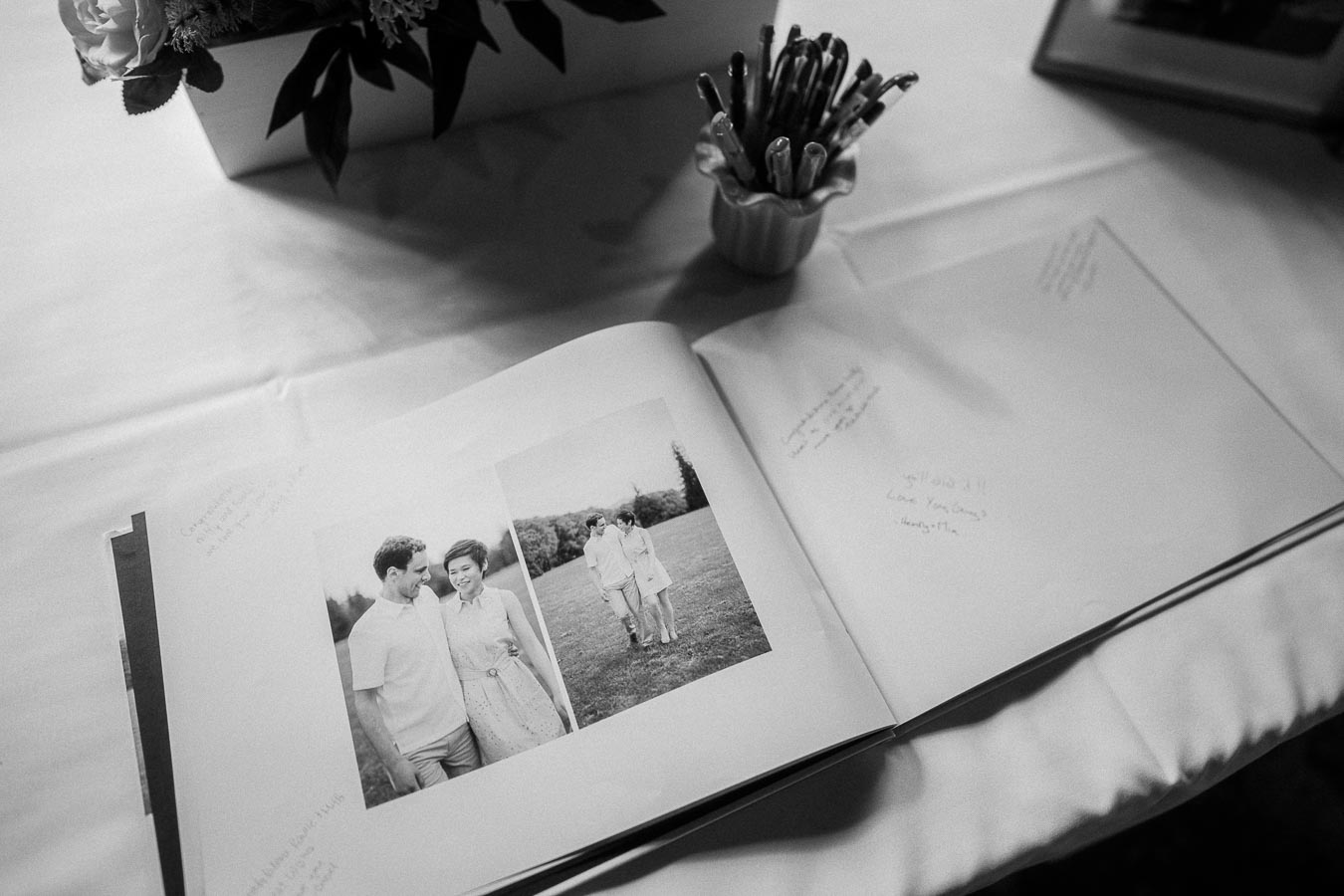 Open wedding guest book with couple portraits, handwritten notes, pens, and flowers on a table