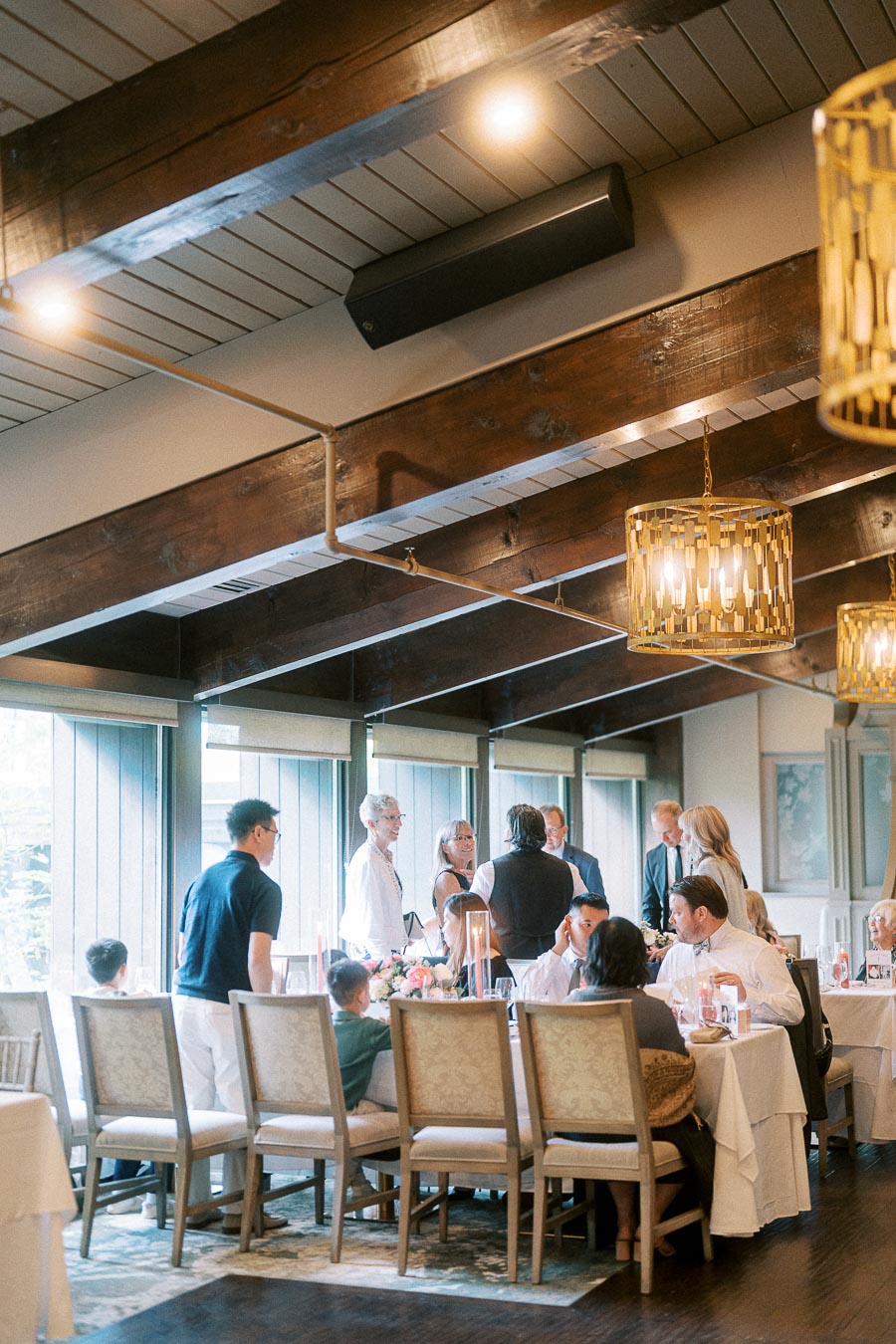 Guests mingle around reception tables beneath wood beams and gold pendant lights at Ancaster Mill.