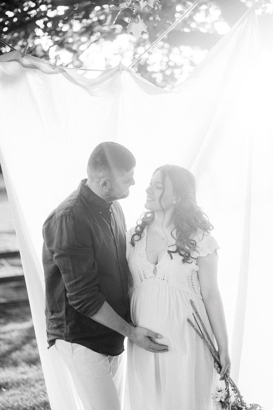 Expectant couple standing together beneath white fabric during maternity session