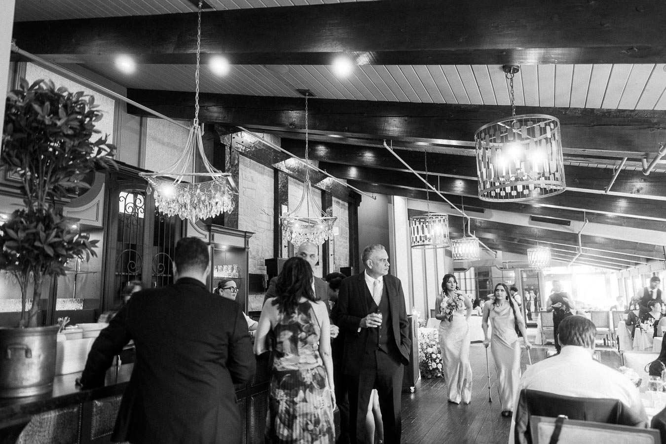 Black-and-white reception room with guests mingling under chandeliers and exposed beams at Ancaster Mill.