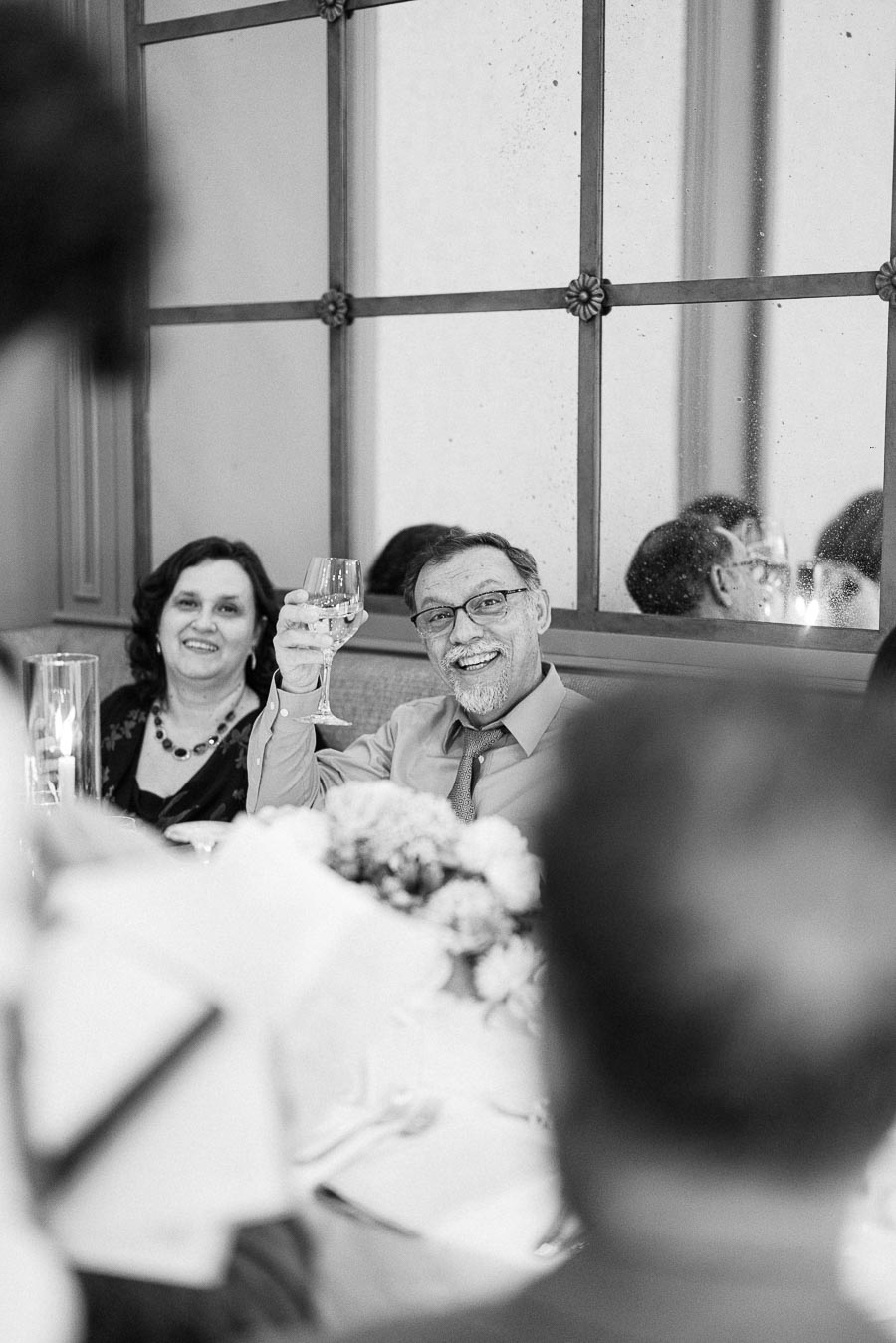 Black-and-white view of a smiling wedding guest raising a glass during the reception meal.