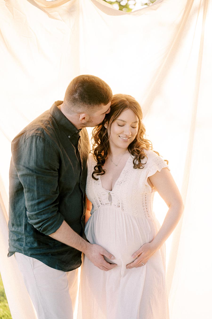 Expectant couple embracing beneath flowing white fabric during maternity session