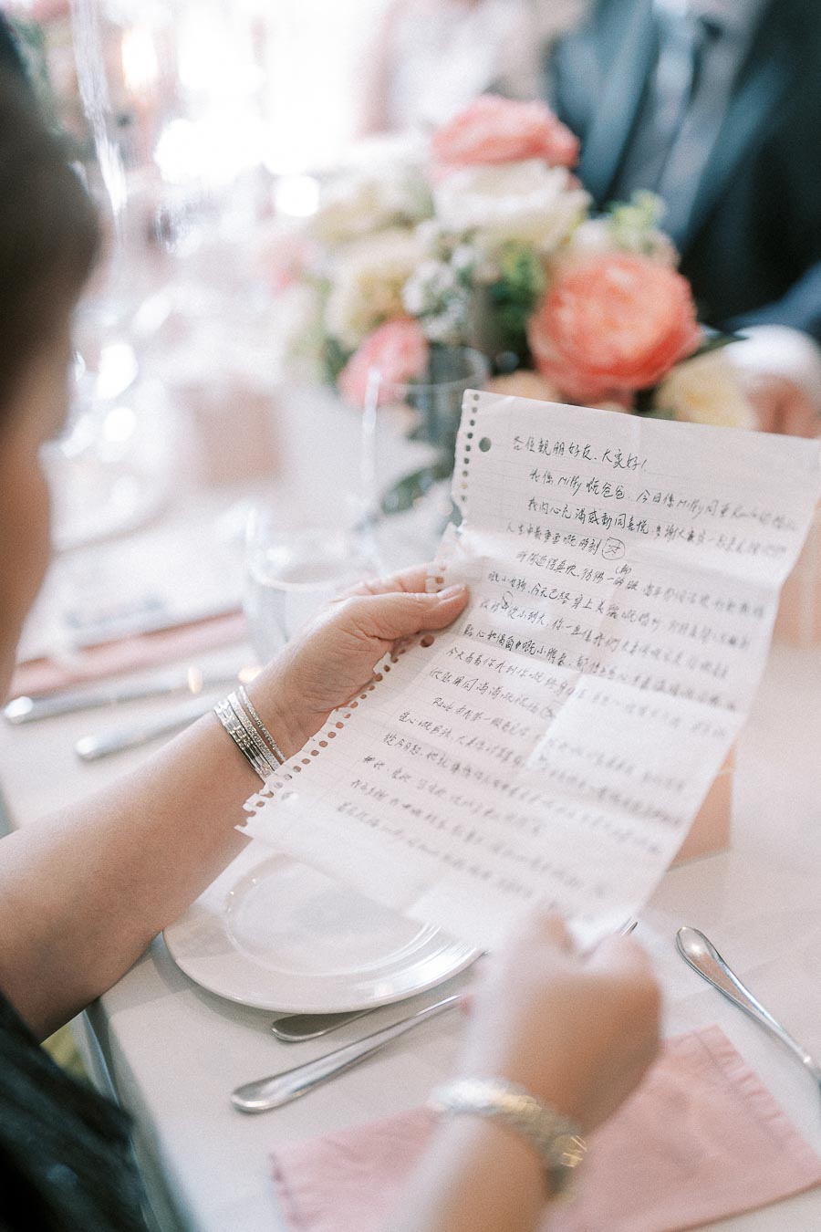 Guest holds a handwritten Chinese letter at a wedding reception table with flowers and place settings.