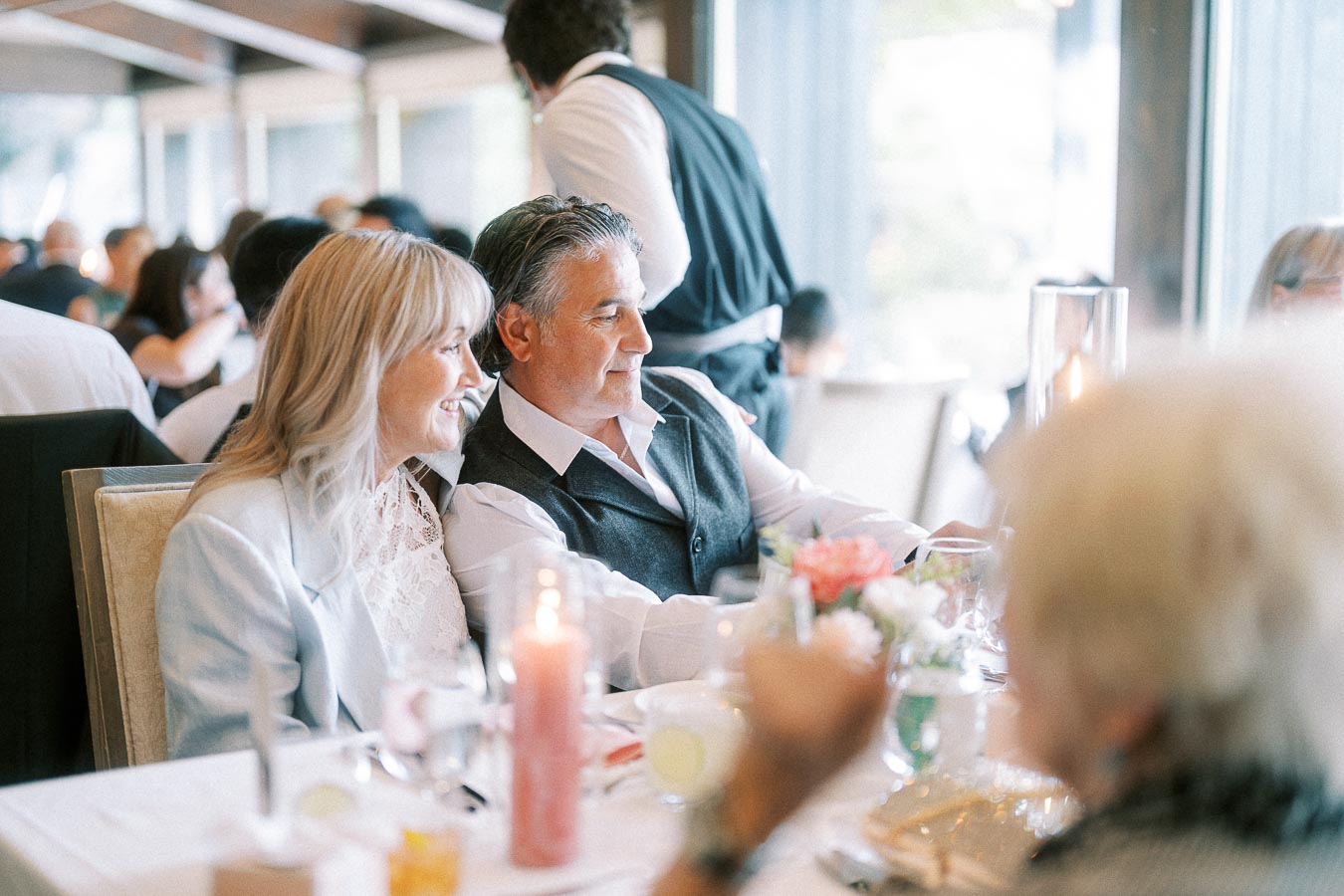 Smiling wedding guests seated at a candlelit reception table near windows at Ancaster Mill