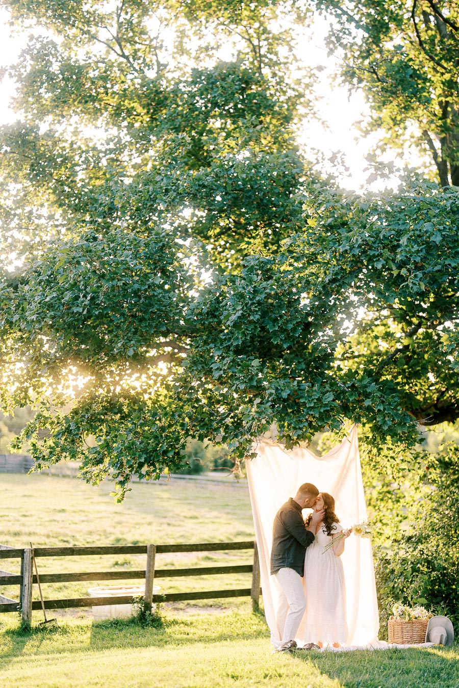 Expectant couple embracing beneath a tree at The Green Acres in Flamborough, Ontario