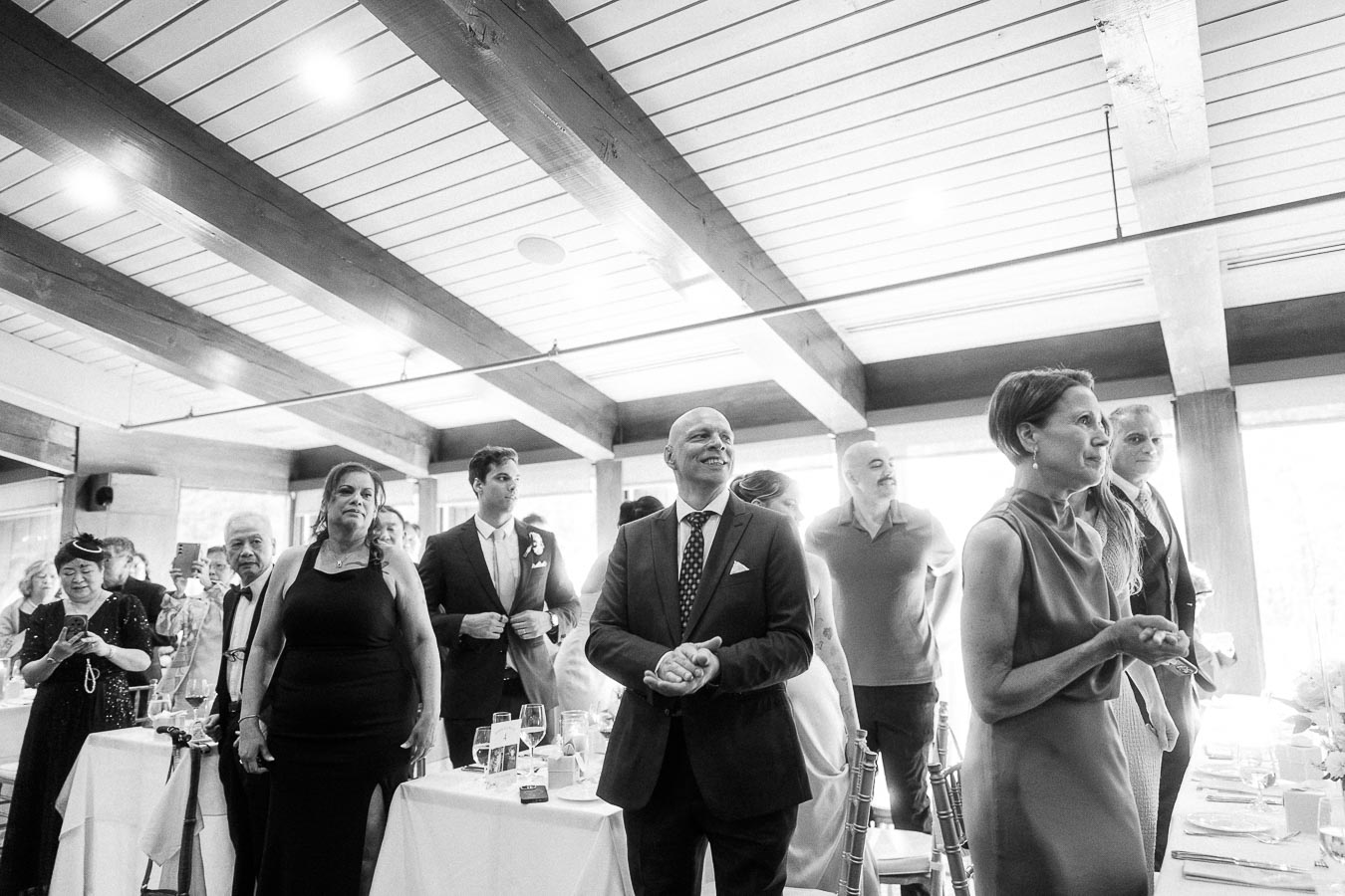 Wedding guests stand between reception tables under wood beams, watching an event at Ancaster Mill.
