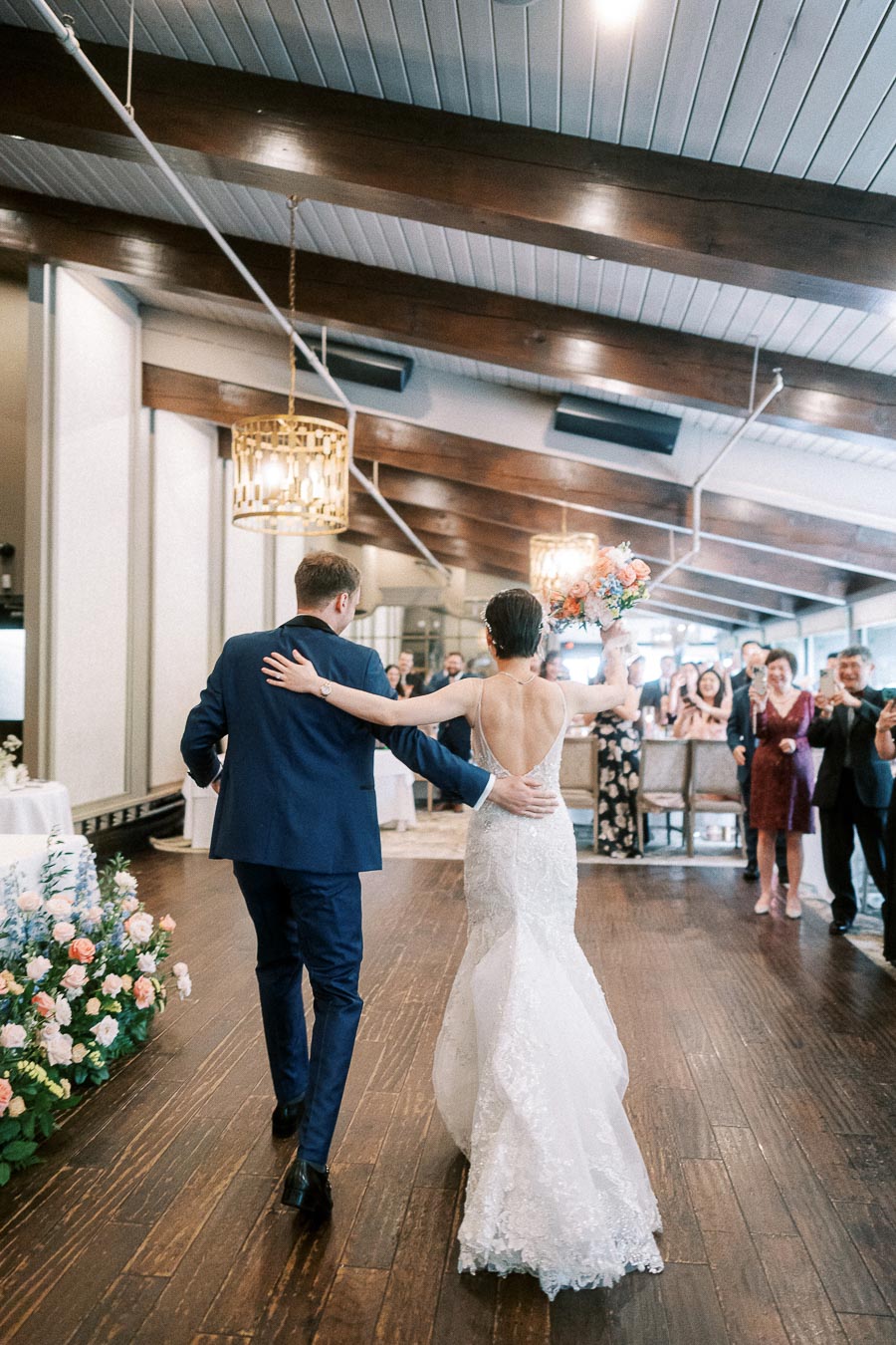 Bride and groom walk into their reception as guests applaud under wood beams at Ancaster Mill.