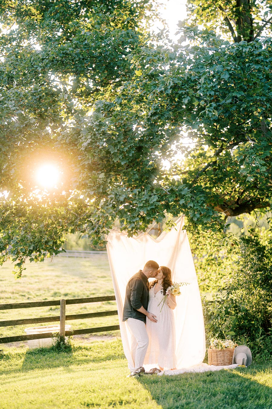Expectant couple kissing under trees during maternity session at The Green Acres